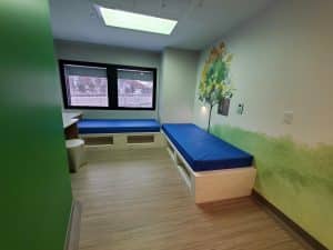 Inside of a room at the mental health unit at Children's Minnesota that has two beds, a desk, and a large window facing trees.