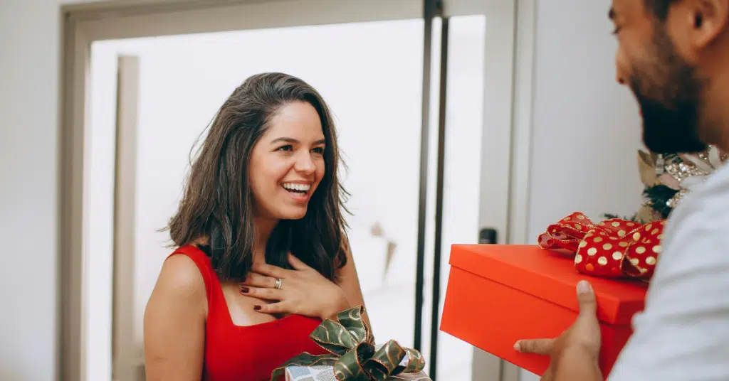 a woman receiving a gift with a joyful expression from a man who is holding a box